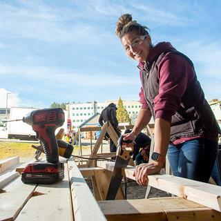 A woman using a hand saw on a construction site. 