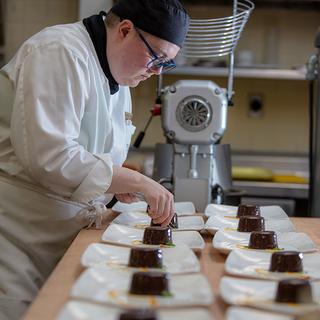 Woman in chef's whites plating food. 